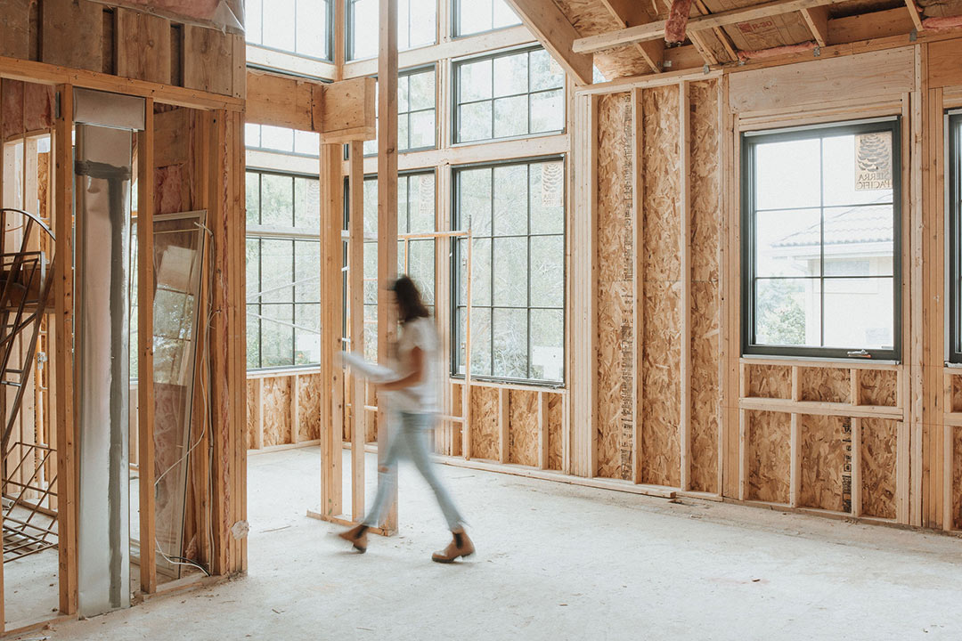 J. Reiko Design + Co. - Should I Hire An Interior Designer - 06 Interior designer, Jenny Murphy of J. Reiko Design + Co, walking through a framed home under construction, representing coordination between interior design and the building process.