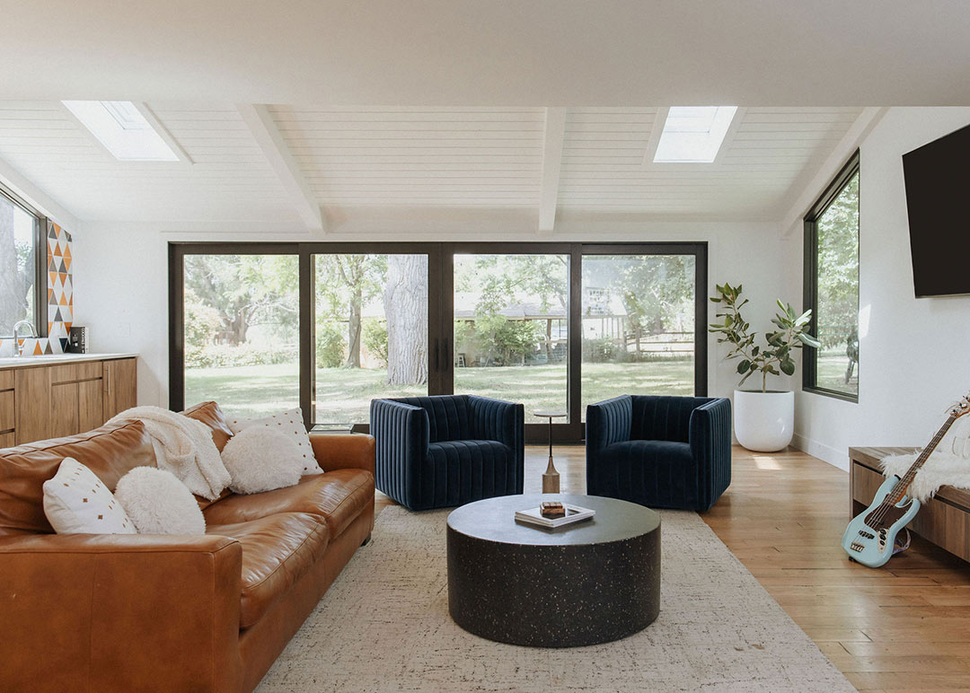 J. Reiko Design + Co. - Asymmetrical Rooms - 03 Basement living space with a round dark coffee table centered between cabinetry, sectional and two accent chairs, balancing function and visual weight.
