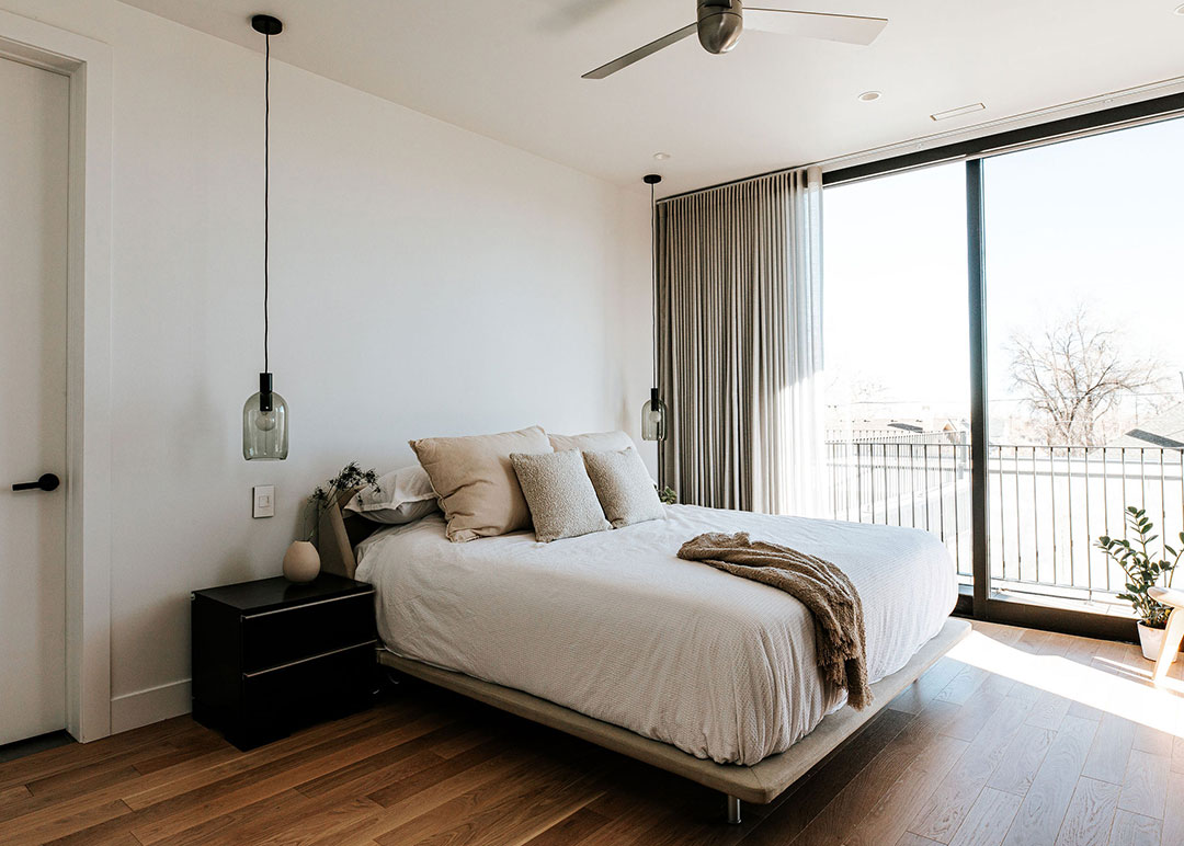 J. Reiko Design + Co. - Japandi Bedrooms - 09 Bright Japandi bedroom with pendant bedside lighting, neutral bedding layers, and sliding glass doors opening to outdoor views.