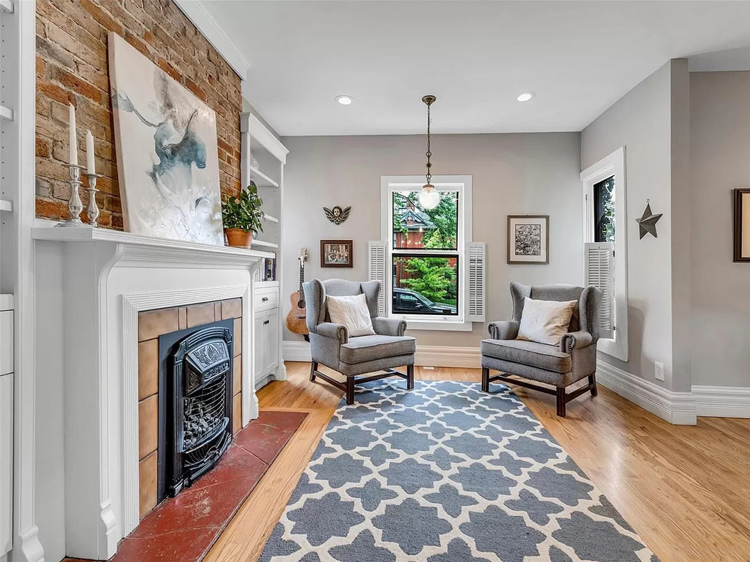 Before living room of Denver Foursquare with fireplace, gray walls, patterned rug, and opened layout lacking historic trim.