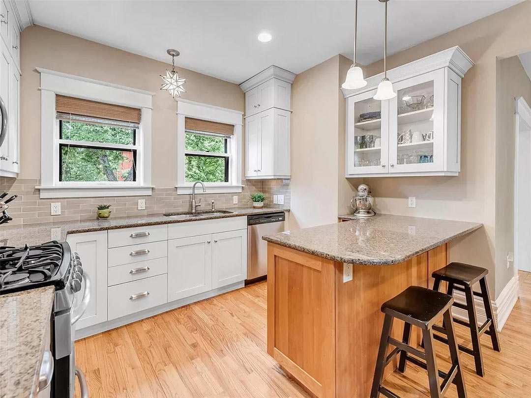 Before kitchen with light gray cabinetry, granite countertops, and peninsula seating disconnected from original Foursquare proportions.