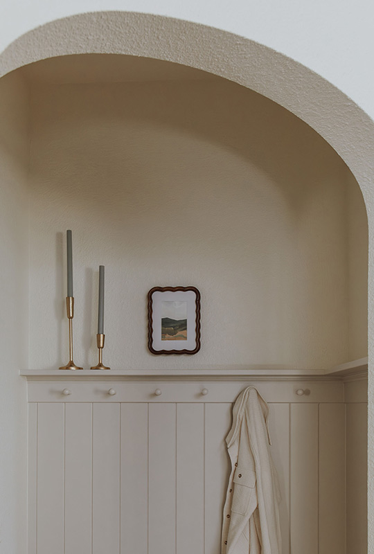 J. Reiko Design + Co. - Modern Colonial Interior Design - 11 Arched niche with beadboard trim, brass candlesticks, framed art, and hanging robe.