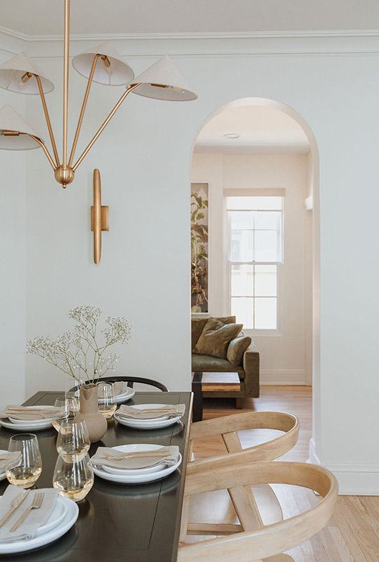 J. Reiko Design + Co. - Modern Colonial Interior Design - 12 Dining table styling with brass chandelier and sconce, set beside a soft arched doorway.