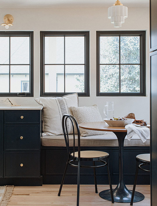 Breakfast nook with black banquette, round pedestal table, and trio of colonial-style windows.