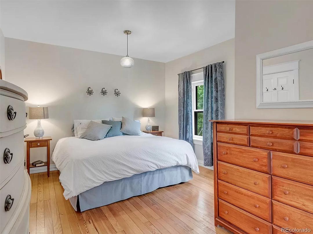 Before bedroom with wood dresser, blue bedding, and simple neutral walls.