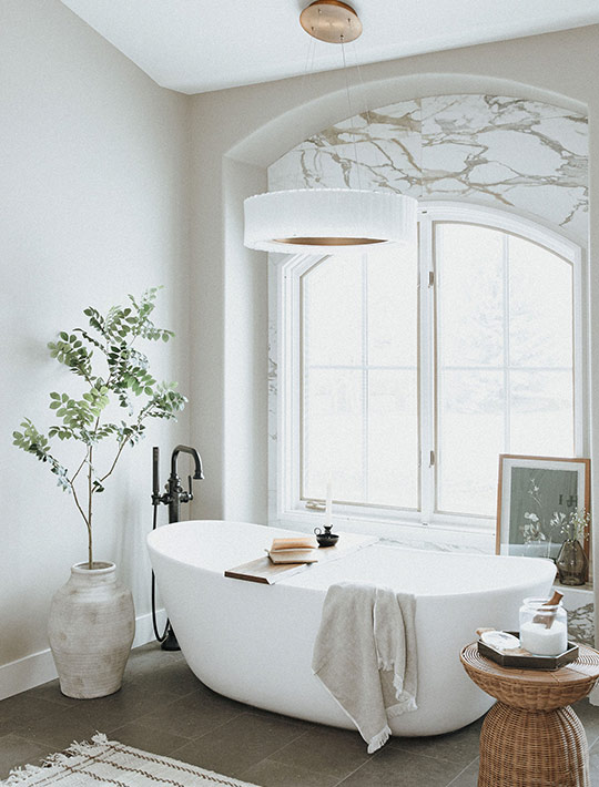 After bathroom with freestanding tub, arched marble detail, and black fixtures.