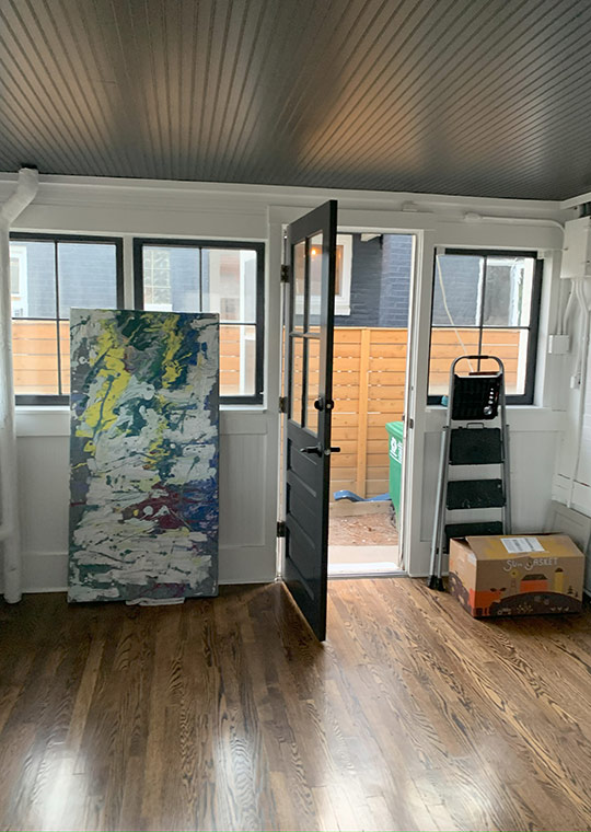 Before entryway with open door, leaning artwork, and in-progress staging.