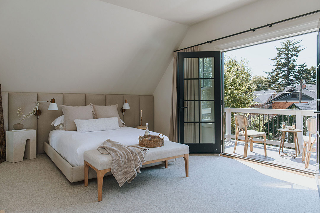 J. Reiko Design + Co. - Modern Colonial Interior Design - 27 Bedroom with upholstered bed and French doors opening to a balcony with bistro seating.