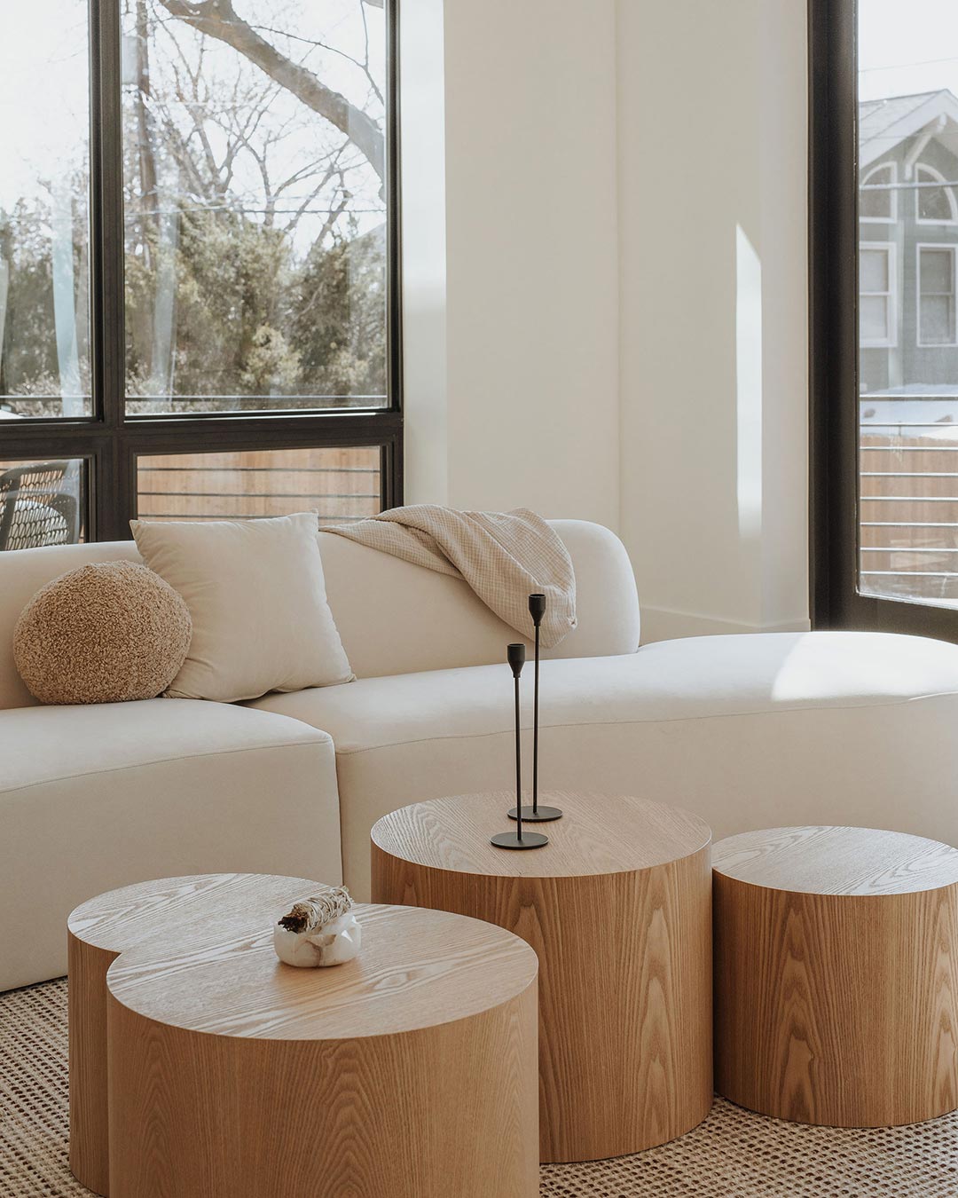 J. Reiko Design + Co. - Quiet Luxury Living Room Ideas - 07 Minimal styling in a neutral living room with natural wood round coffee tables with minimalist candle sticks, and shearling accent pillow on a creamy neutral sectional.