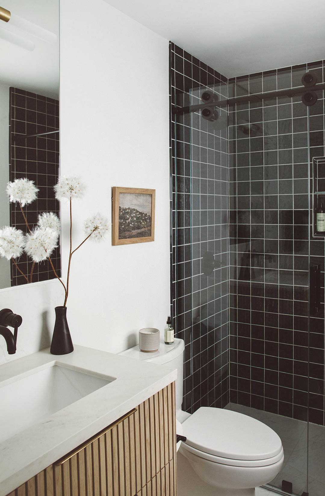 Minimalist bathroom vanity with fluted wood cabinetry, wall-mounted black faucet, white quartz countertop, and modern mirror with brass sconce lighting. Design by Jennifer Murphy of J. Reiko Design + Co