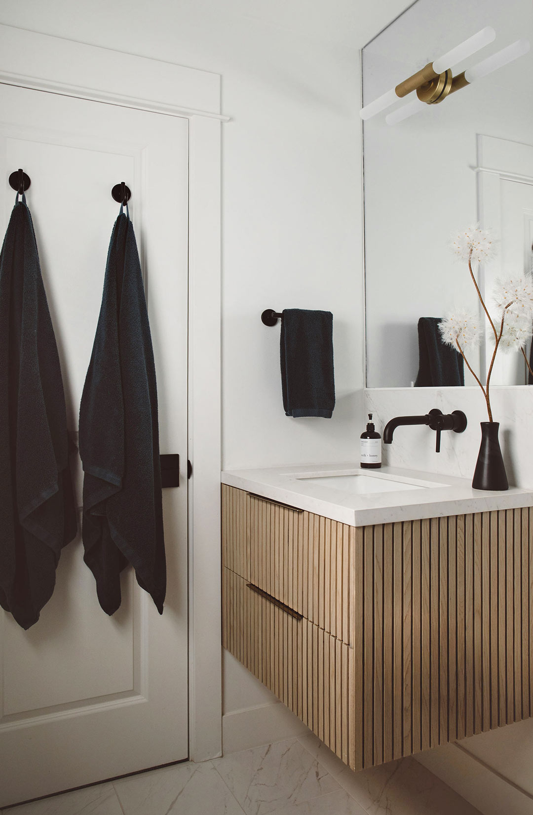 Modern bathroom with black square tile shower, glass shower enclosure, floating wood vanity with fluted drawer fronts, and white quartz countertop.